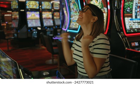 A joyful young adult woman celebrates winning at a casino slot machine. – Ảnh có sẵn