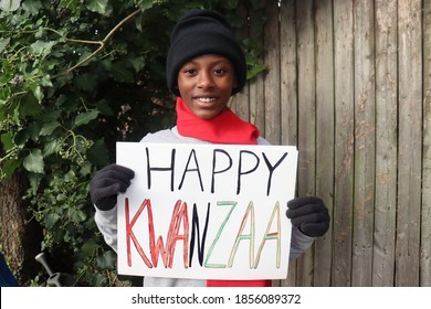Kid in winter clothing holding Happy Kwanzaa sign outdoors: stockfoto