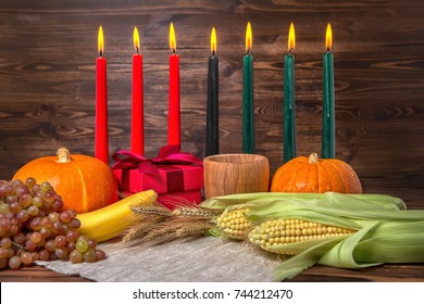 Kwanzaa festival concept with seven candles red, black and green, gift box, pumpkins, ears of wheat, grapes, corns, banana, bowl and fruits on wooden background, close up: stockfoto