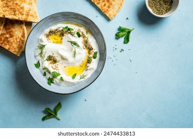 Labneh yogurt cream cheese with olive oil, herbs and zaatar on blue, copy space. Traditional arabian or middle eastern homemade labneh dip with pita bread for breakfast. Arabic Cuisine.: zdjęcie stockowe