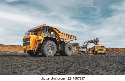 Large quarry dump truck. Big yellow mining truck at work site. Loading coal into body truck. Production useful minerals. Mining truck mining machinery to transport coal from open-pit production 库存照片