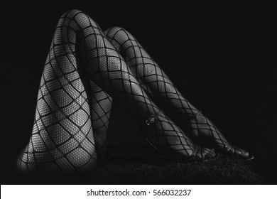 Low key greyscale photo of sexy slim beautiful legs in black net tights and high heels shoes against black background, horizontal view : photo de stock