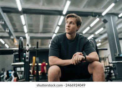 フィットネス男性のチェックの低角度の肖像画モダンなジムでのトレーニングの時間、バーベルで運動する時間を待っています。スポーツクラブで若い男のトレーニング。健康的なライフスタイル、身体活動の概念。の写真素材