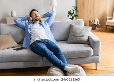 A man is comfortably seated on a couch in his living room, appearing relaxed and at ease. The room is well-lit with natural light, and the man seems to be enjoying a moment of rest and relaxation. Foto stock