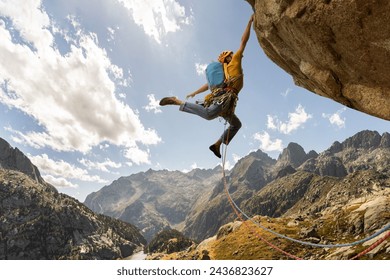 A man is climbing a mountain with a blue backpack. He is wearing a yellow jacket and is jumping off a cliff Stockfoto