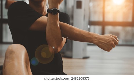 검은 운동복 차림의 남자는 피트니스 체육관에서 웨이트 트레이닝을 하기 전에 어깨와 어깨를 뻗고 팔을 뻗고 준비 운동을 합니다. 건강한 스포츠 라이프 스타일은 근육, 건강 및 피트니스 개념을 구축합니다. 스톡 사진