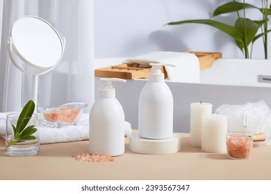 Many bathroom supplies featured on beige table with glass container of pink himalayan salt and unlabeled pump bottles. Himalayan salt is becoming increasingly popular due to its therapeutic properties Foto stock