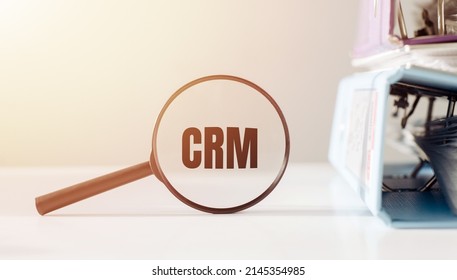 Magnifying glass with text CRM on white background near office folders.: zdjęcie stockowe