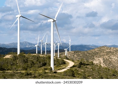カタルーニャ州の風景の中に高く立つ雄大な風力タービンは、タラゴナ地域のスペインの空の下に山があり、持続可能なエネルギーソリューションを強調していますの写真素材