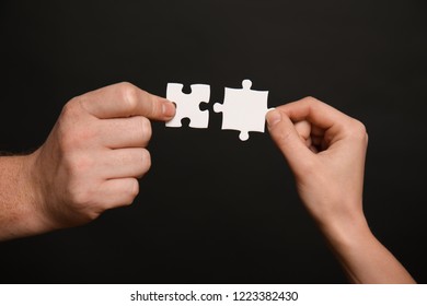 Male and female hands with pieces of puzzle on dark background Foto stock