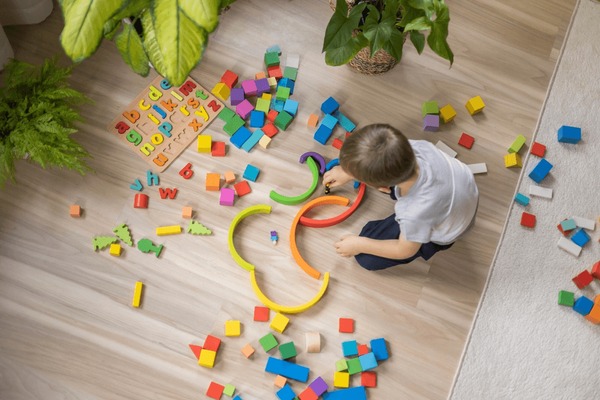 Niño masculino jugando arco iris Montessori madera material natural de desarrollo temprano juguete en el suelo en casa. El laberinto de construcción de niños pequeños con bloques de cubos de ecología de arco curvo de color Foto de stock