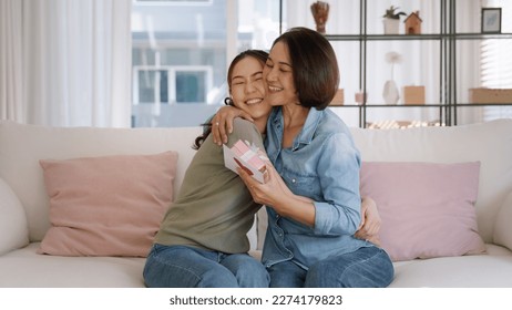 May Mother's day young adult grown up child cuddle hug give flower gift box red heart card to mature middle aged mum. Love kiss care mom asia people sitting at home sofa happy smile enjoy family time. Stock Photo