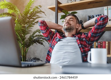 Middle aged man resting in front of laptop screen at his work place, with arms behind the head. Millennial freelancer worker leaning back at workplace, enjoying his job, feeling pleased and satisfied Adlı Stok Fotoğraf