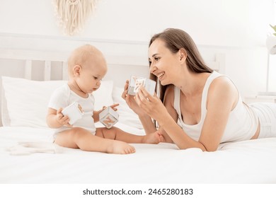 mamá y bebé juegan con cubos de juguetes de madera divirtiéndose juntos en la cama en un dormitorio luminoso, maternidad feliz con licencia de maternidad, amor y cuidado materno, desarrollo temprano del niño. Foto de stock