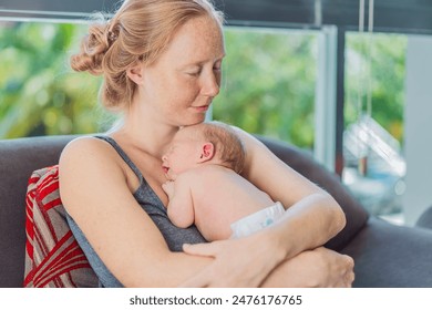 自宅でソファでリラックスしている新生児の赤ちゃんを持つママ。この優しい瞬間は、快適で愛情のある家庭環境の中で母子の絆を強調していますの写真素材