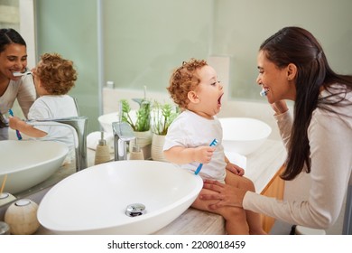 Mom teaching baby to brush its teeth, on the bathroom counter in home and a clean smile on her face. Healthy oral hygiene for kid means using child friendly toothpaste, toothbrush and dental routine Stock Photo