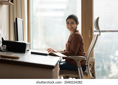 Modern day worker. Portrait of happy biracial business woman freelancer sit by computer at comfy workplace at corporate workspace or at home. Smiling young indian lady office employee look at camera Stockfoto