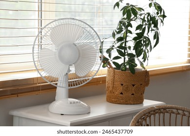 Modern electric fan with houseplant on commode at home Stock-foto