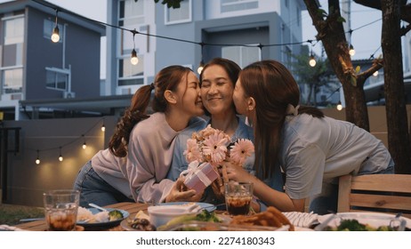 Mother's day two young child cuddle hug give flower gift box to mature mum. Love kiss mom asia people middle aged adult at home cozy dining table night dinner party happy smile enjoy relax warm time. Stock Photo