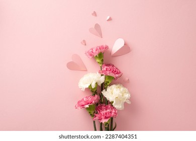 Mother's Day present idea. Top view of carnation flowers and heart-shaped papers on a pastel pink surface Stock Photo