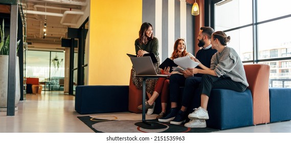 Multicultural businesspeople working in an office lobby. Group of happy businesspeople smiling while sitting together in a co-working space. Young entrepreneurs collaborating on a new project. ஸ்டாக் ஃபோட்டோ