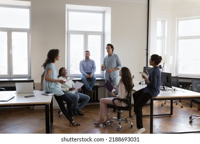 Multiracial staff members, colleagues talking about new project, brainstorming, gathered in coworking workspace. Share knowledge, information or ideas, cooperate, take part in morning briefing Foto stock