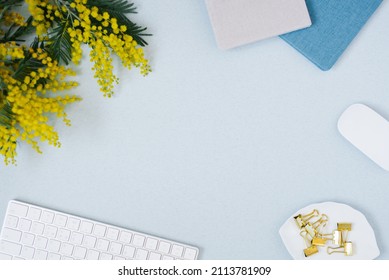On a blue flat lay background with a yellow mimosa flower, keyboard notepad and stationery clips, a female floral desktop. The concept of a stylish spring morning. top view and copy space Stockfoto