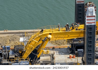 Редакционная стоковая фотография: Panama Canal, Panama - 23 January 2024: Workers standing on the arm of a large excavator on an industrial barge used to dredge the Panama Canal to remove silt and dirt.
