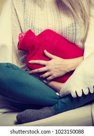 Painful periods and menstrual cramp problems concept. Woman having stomach cramps sitting on cofa feeling very unwell holding hot water bottle to feel some relief Foto de stock