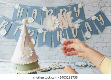 Person holding a birthday hat and daisy flower decoration at a celebration with "Happy Birthday" banner in the background. स्टॉक फ़ोटो