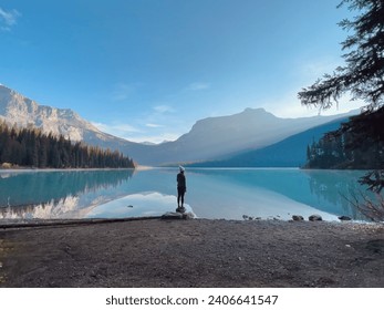 早朝の日差しの中、湖の上の岩の上に一人で立っている人カナディアンロッキーの写真素材