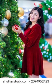 Portrait beautiful young asian woman red dress costume and Christmas greeting picture parcel decoration on Christmas tree light circular bokeh background Decoration During Christmas and New Year. Stock Photo