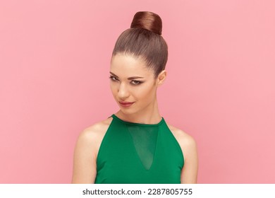 悪魔植物を持ったり、いたずらを準備したり、緑のドレスを着て、ずるそうな顔の表情でカメラを見てパンの髪型とずるそうな女性のポートレート。ピンクの背景に屋内スタジオのショット。の写真素材