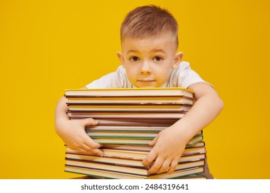 Retrato de un niño lindo sentado con una pila de libros. Fondo de estudio amarillo con espacio de copia. Educación y desarrollo temprano de los niños.  Foto de stock