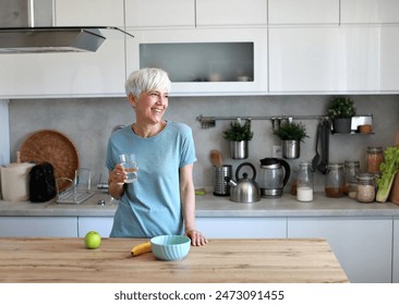 Retrato de una mujer madura adulta feliz de mediana edad que sostiene un vaso y agua potable y que tiene un desayuno saludable después del entrenamiento de ejercicio físico por la mañana en casa Foto de stock