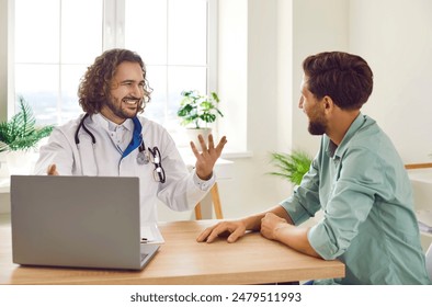 Portrait of a happy smiling young man patient in office listening to recommendations of friendly male doctor sitting at the desk in clinic during medical examination. Health care concept. Foto stock