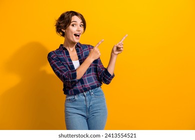 Portrait of impressed ecstatic girl with short hair wear checkered shirt directing at sale empty space isolated on yellow color background Foto stock
