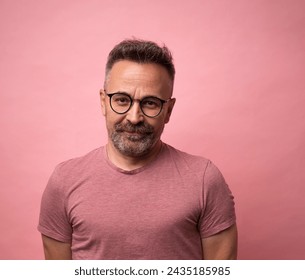 Стоковая фотография: Portrait of mature 50s smiling caucasian man dressed in casual red t-shirt with glasses on calm attractive face isolated on pink studio background