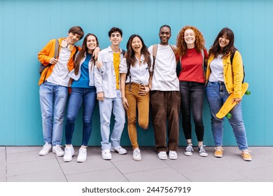 Portrait of seven young student friends leaning on blue wall. Diverse teenage classmates looking at camera standing at university campus. Education and youth concept. Foto stock