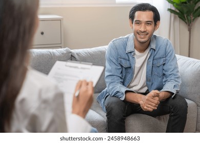 Psychology, depression. Happy smile asian young man patient mental therapy explain symptom with psychologist while doctor woman taking notes at clinic. Psychologist with sick mental health person. 库存照片
