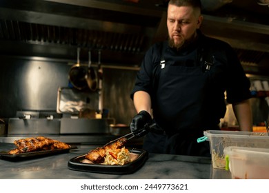 in a professional kitchen the chef puts ribs on a plate near the table and decorates them on a plate Foto stock