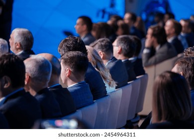 Professionally dressed audience members at a corporate event are focused on a presentation, illustrating engagement and professional development in a business setting. 庫存照片