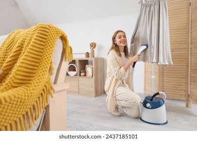 Hübsche junge Frau dampfende Kleidung mit modernem Bekleidungsdampfer zu Hause – Stockfoto