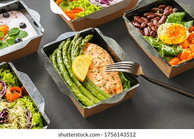 黒いテーブル背景にフォークと日常食事計画宅配便として、魚や野菜の弁当箱の健康食のケータリングメニューを用意。 コンテナを持ち去る注文のコンセプト。の写真素材