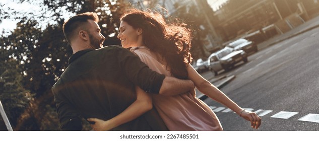 Rear view of beautiful young couple embracing and smiling while walking by the city street Foto stock