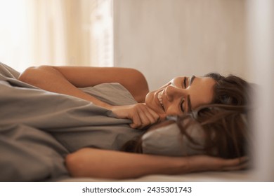 Relax, happy and woman in bed at her home on weekend morning for calm, rest or sleeping. Confident, smile and young female person laying with duvet blanket in bedroom at apartment in Canada. Stockfoto