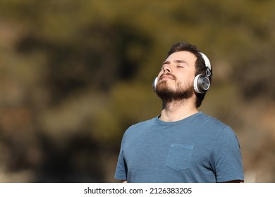 Relaxed man breathing fresh air and meditating listening audio guide with headphones in nature: stockfoto