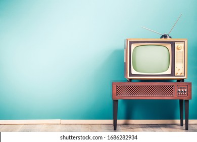 Retro old outdated classic television receiver with TV antenna from circa 60s of XX century on wooden stand with amplifier front gradient mint blue wall background. Vintage style filtered photo Stock Photo