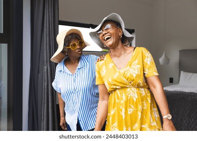 アフリカ系アメリカ人女性とバイラシアル女性の先輩は、休暇の楽しい瞬間を共有しています。どちらも夏の装いで、つばの広い帽子とサングラスでスタイリッシュに着られ、幸せを醸し出しています。の写真素材