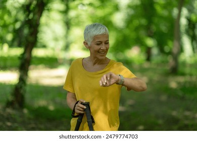 Senior woman checks smartwatch after nordic walking in the park for fitness tracking. – Ảnh có sẵn